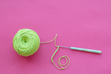 Top view on crochet hook and green jute thread ball on a pink background with copy space. Eco-friendly knitting