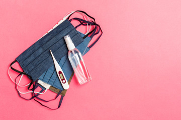 Top view of handmade cotton masks, alcohol hand sanitizer and digital thermometer on pink...