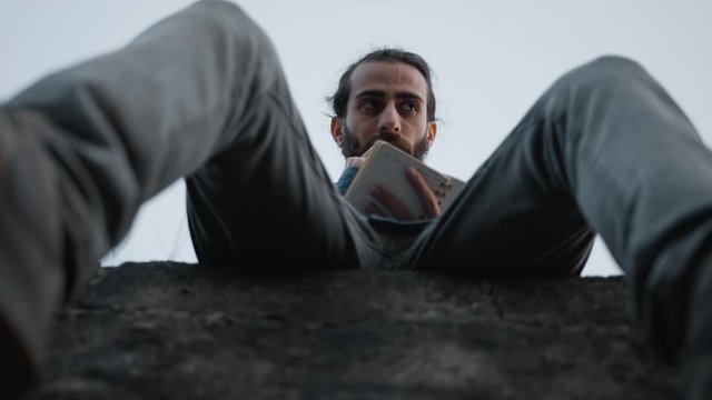 Young handsome man sitting on the wall, writes his ideas. He's happy to find a good idea. Shooting from the bottom up.