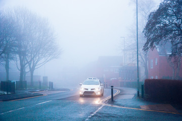 A white taxi car moving in a fog in a city - concept of a dangerous hazardous driving conditions, limited visibility