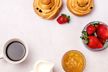 Obraz na płótnie Canvas Tasty Breakfast Freshly Baked Buns with Raisins and Cinnamon Cup of Black Coffee Cream Ripe Strawberry and Orange Jam in Glass Bowl Top View Copy Space