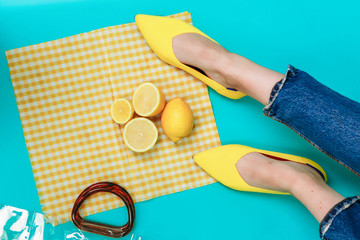 beautiful female legs are dressed in stylish yellow shoes without a heel. Light yellow summer sandals on a blue background against the background of a handbag and bright lemons