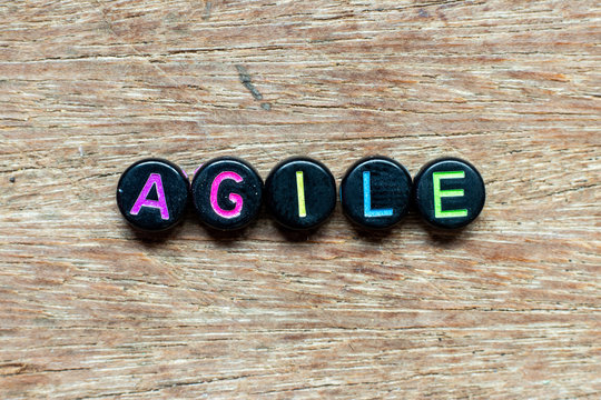 Black bead with color letter in word agile on wood background