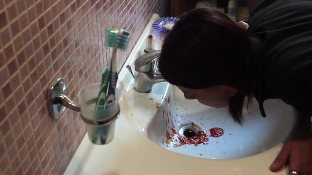 woman spitting coughing blood in the bathroom sink getting dirty with blood and worries