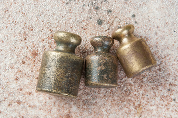 Three antique bronze weights for scales on concrete background.