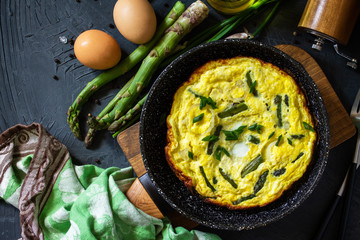 Healthy Asparagus Omelet. Egg omelet with asparagus and onions in a cast iron skillet on a stone countertop. Top view flat lay background.