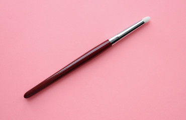 A brush made of wood, with white nap, for applying makeup, blending eye shadow, on a pink background. Beauty, fashionable women's accessory, tassel.