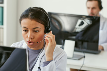 Young woman wearing headphones working on computer she answering on phone calls in medical call...