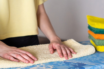 Hands fold a ironed towel, a stack of ironed things. Homework concept, housewife