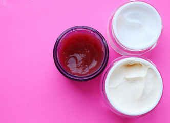 three glass jars with cream for the body, face, on a bright pink background. View from above. Cream texture. Home care, care, cosmetics. Natural cream, affordable care.