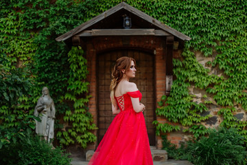 Obraz na płótnie Canvas Attractive redhead tattooed woman in red dress and diadema posing on blurred medieval castle background