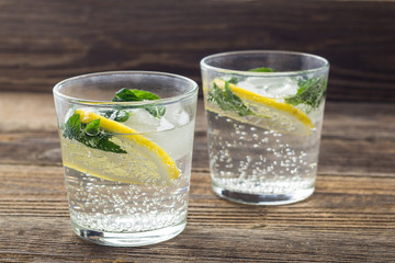 Two glasses of lemonade with lemon, mint and ice cubes on wooden background. Summer drink