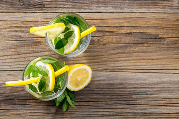 Water with lemon and mint in a glass on wooden background. Summer fresh lemonade drink
