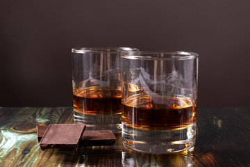 
Two glasses with whiskey and dark chocolate. Dear elite alcohol on a dark brown background. Alcoholic drinks.
