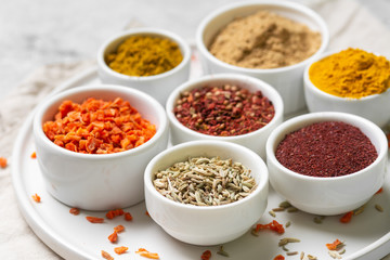 Spices and condiments in white bowls on a light gray table. Turmeric, ginger, curry, fennel and sumac in white bowls. Spices close up with space for text