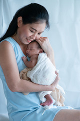 Obraz na płótnie Canvas Asian mother is holding newborn baby in her arms, tender embrace of mother, happy mother and baby enjoy spending time together