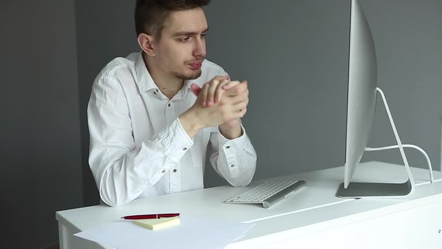 Young man in white shirt working at the desktop with a computer in office. Worker on grey background