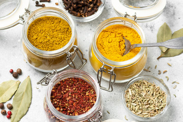 Spices and condiments in glass jars on a light gray table. Spices close-up with space for text. The view from the top