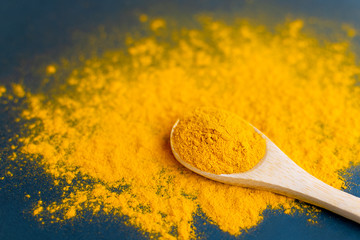 Close-up turmeric powder in wooden spoon at scattered curcuma.