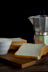 Homemade bread slides on a wooden chopping board in the kitchen in the house on a black background and aluminum Moka pot coffee maker and copy space. High carbohydrate food concept.