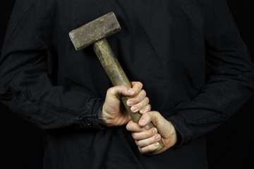 A man holds a sledgehammer, a hammer behind his back on a black background