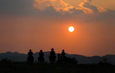 Silhouette of western riders against amber colored sunset