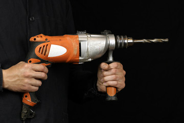 Man's hands hold an electric drilling machine, drill on black background