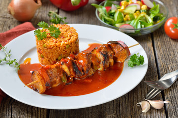 Deftiger Schaschlik-Spieß in pikanter Sauce mit Djuvec-Reis und gemischtem Beilagensalat serviert  – Hearty shashlik skewer in a spicy sauce with Djuvec rice and mixed side salad