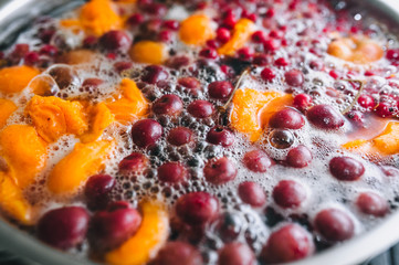 Fototapeta na wymiar Fresh fruits are boiled in boiling water in a metal pan on a stove with bubbles and foam close-up. Cooking a delicious compote of apricot, apples, cherries, raspberries. Photography, concept.