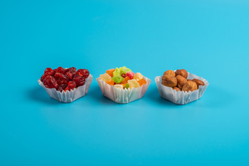 A serving of assorted candied fruit, dried cherries and hazelnuts in paper muffin cups on a blue background.