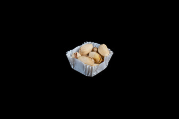 A serving of pistachios in a paper muffin cup on a black background.
