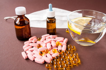 Medical still life: tablets, fish oil, medical mask, a mug of water with lemon and medicine in bottles on a brown background