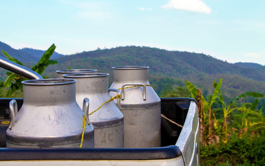 A milk can or buckets place on a pickup truck which parks on a country road, resting on the way back home. Natural countryside  background.