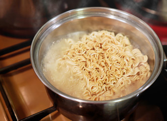 Instant noodle is cooking in boiling water in stainless pot on gas stove , cheap or budgeted food for survive during economic crisis concept ,selective focus