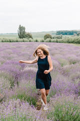 Beautiful woman funny walk on the lavender field on sunset. Beautiful girl in dress stand and flying long hair on purple lavender field. Soft focus. Enjoy the floral glade, summer nature. Hairstyle.