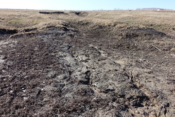 Harsh nature landscape and road through fields and mountains along the riverbed for off-road SUV with puddles and mud. Spring background with wet earth and snow and slush.