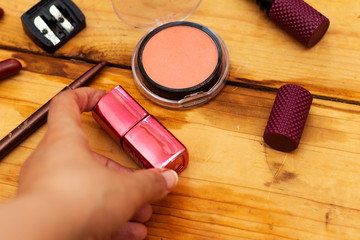 Obraz na płótnie Canvas hand holding nail bottle, pink blush, variety lipstick and lip gloss, mascara brush on wood table