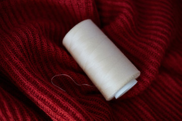 Fototapeta na wymiar Bobina de hilo blanco roto de algodón sobre tejido de lana rojo