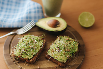 Toast with microgreens and guacamole on top. Rye toasted bread on wooden board. Healthy food at home. Vegan food concept