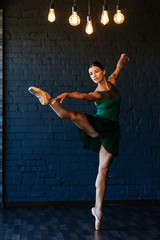 Modern ballet dancer performing a ballet exercise on a dark studio background. Dancer in a green...