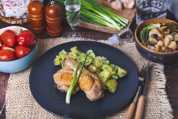 Chicken with potatoes, salted tomatoes and pickled mushrooms. In the background is a glass of vodka, a decanter, a salt shaker, onion and garlic. Rustic style.