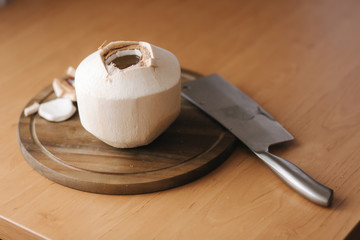 Open coconut with machete knife on wooden board at home - obrazy, fototapety, plakaty