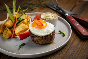 Beef medallions with egg, potatoes and peppers on a wooden background