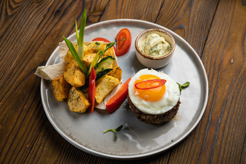 Beef medallions with egg, potatoes and peppers on a wooden background