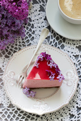 A berry mousse cake with chocolate base and juice jelly, decorated with lilac flowers, served with coffee.