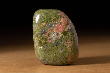 Polished Unakite gemstone from South Africa over a wooden table