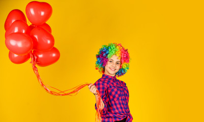 small girl in periwig. valentines day party. child wear rainbow wig hair yellow background. happy kid hold party balloons. heart balloons for love day. surprise for valentine. colorful and bright