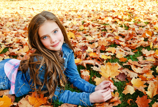 Autumn portrait of adorable smiling little girl child preteen lying in leaves in the park
