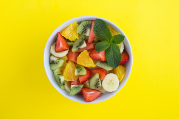 Fruit  salad in the white  bowl In the center of  the yellow  background. Top view. Copy space.