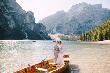 Bride and groom sailing in wooden boat, with oars at Lago di Braies lake in Italy. Wedding in Europe - Newlyweds are standing embracing in a boat.